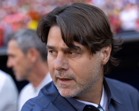 A man with longish brown hair and a salt and pepper beard looks on from the sideline before a match